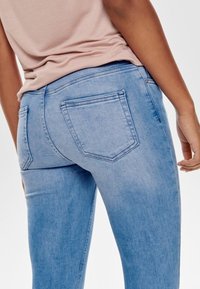 Ljusblå jeans i denim med en figurnära passform, som har två bakfickor och en enkel design. Tyget verkar något slitet.