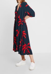 Námořnické šaty s červeným listovým vzorem, výstřih do V, krátké široké rukávy, stahovaný pas a splývavá sukně. V kombinaci s bílými platformovými teniskami.