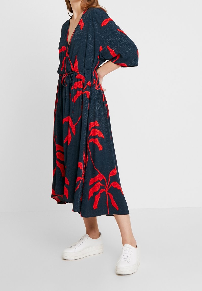 Námořnické šaty s červeným listovým vzorem, výstřih do V, krátké široké rukávy, stahovaný pas a splývavá sukně. V kombinaci s bílými platformovými teniskami.