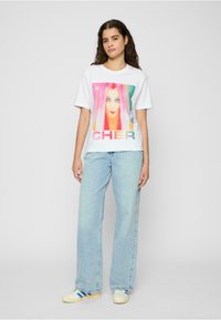 Hvit bomull t-skjorte med en fargerik grafikk av Cher med rosa hår, sammen med lyseblå denimjeans og kremfargede sneakers.