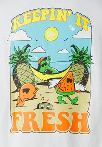 Camiseta blanca con frutas de dibujos animados coloridas: una naranja, una sandía y un aguacate en una playa con piñas y un sol arriba. El texto dice "MANTENIÉNDOLO FRESCO".