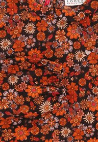 Bloemstof met oranje, rode en gedempte blauwe bloemen op een zwarte achtergrond. Inclusief geplooide textuur en een zilveren hartaccent.