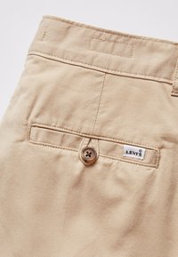 Pantalon en coton beige avec une poche arrière plate, une fermeture à un seul bouton et une étiquette Levi's blanche cousue au-dessus de la poche.
