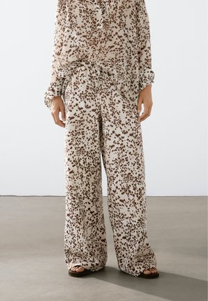 Lehký béžový set z látky, který obsahuje volně střiženou košili s dlouhými rukávy a široké kalhoty, oboje s hnědým tečkovaným vzorem.