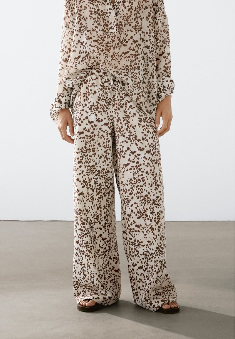 Lehký béžový set z látky, který obsahuje volně střiženou košili s dlouhými rukávy a široké kalhoty, oboje s hnědým tečkovaným vzorem.