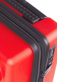 Red hard-shell suitcase featuring a textured matte finish, double black zipper, and angled corners. Includes black accents and a combination lock.