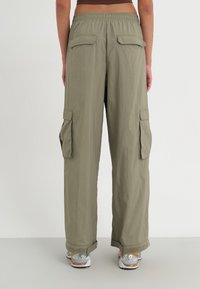 Spodnie cargo w jasnooliwkowym kolorze, z luźnym krojem, elastycznym paskiem w talii i kieszeniami po bokach. Tkanina ma gładką teksturę.