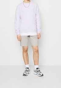 Sweatshirt lilas, T-shirt blanc en dessous, shorts gris clair et chaussures de sport argentées avec accents en teal. Design simple avec encolure ronde.