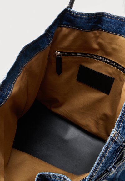 Vue intérieure d'un sac fourre-tout en denim ouvert avec doublure en tissu marron, poche intérieure zippée et étiquette noire.