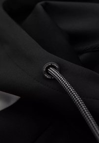 Tessuto nero con una superficie liscia, caratterizzato da un occhio decorativo nero con logo e un cordino intrecciato con una superficie a motivi.
