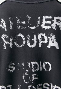 Sweatshirt nero con lettering bianco testurizzato che recita "ATELIER YOUNG STUDIO OF ART & DESIGN" in uno stile invecchiato.