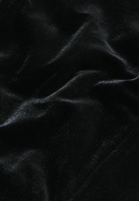 Tissu en velours noir doux avec des plis délicats et des reflets subtils créant une texture lisse et légèrement brillante.