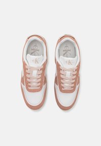 Paire de baskets en daim blanc et marron clair avec des lacets roses, marquage Calvin Klein sur la languette et la semelle intérieure, photographiées de dessus.