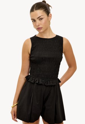 Robe courte noire sans manches avec corsage smocké, peplum volanté et shorts structurés. Le tissu semble léger avec une texture lisse.