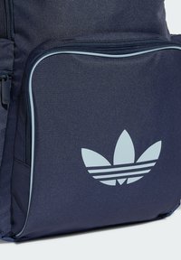 Marinblå ryggsäck i texturerat tyg med en ljusblå dragkedja, accentuerande piping och en framträdande ljusblå Adidas-logotyp med ränder.