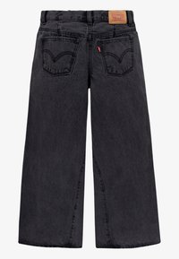 Jeans en denim noir à jambes larges avec une texture délavée, dotés de deux poches arrière avec un motif de couture distinctif et d'un patch en cuir de marque.