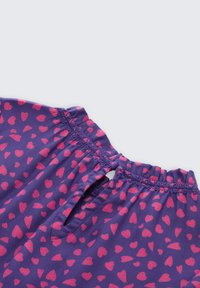 Lila Stoffoberteil mit kleinem pinken Herzmuster, mit einem gerafften Ausschnitt und einem Schlüssellochverschluss hinten. Weicher Stoff.