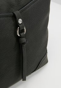 Sac à main en cuir gris foncé avec une surface texturée, des accents en métal argenté, une sangle en cuir décorative et des coutures contrastantes.