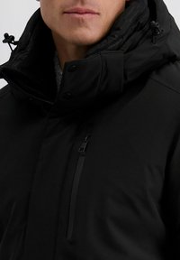 Schwarze isolierte Jacke mit hohem Kragen, durchgehendem Reißverschluss und verstellbarem Kapuzen. Verfügt über eine Seitentasche und eine glatte Textur.