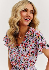 Kwiecista sukienka w pastelowych kolorach z krótkimi falbaniastymi rękawami, z dekoltem w kształcie litery V i wiązaniem w talii. Uzupełniona perłowym naszyjnikiem.