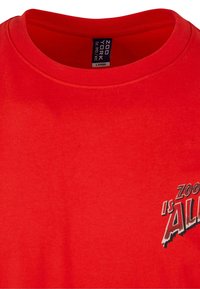 Rød bomulds t-shirt med rund halsudskæring, korte ærmer og et grafisk print på forsiden, der står "ZOO YORK is ALL" i kontrastfarver.