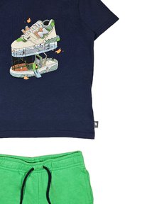 T-shirt blu navy con una grafica dettagliata di una sneaker, abbinato a pantaloni corti verdi con vita elastica e stringente.
