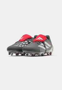 Gray soccer cleats with red accents and white stripes. Features a textured surface and a fitted design for improved grip and performance.