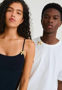 Top negro de canalé con un broche de mariposa dorada en el hombro izquierdo; camiseta blanca con un broche de mariposa a juego en el hombro derecho.