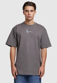 Siva oversized majica izrađena od pamuka, s kratkim rukavima i okruglim izrezom. Na prsima ima bijeli potpisani grafički uzorak.