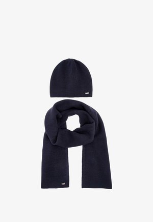 Dark blue knitted hat and matching scarf with small metal brand tags on a white background.