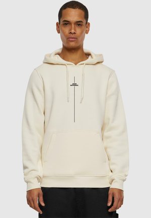 Hoodie crème avec une poche avant, capuche réglable à cordelette, et impression de logo noire au centre. Tissu doux et texturé.