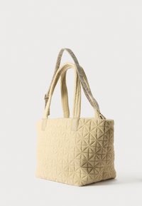 Sac fourre-tout rembourré en tissu beige clair avec un motif de diamants texturé. Dispose de deux poignées solides et d'une bandoulière réglable à motif.