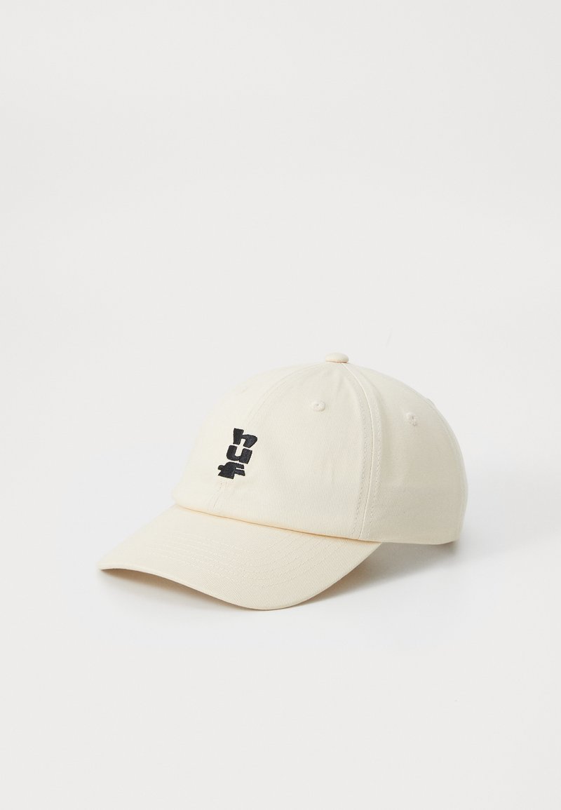 Cream-colored baseball cap with a rounded crown, curved visor, and black embroidered logo on the front. Made of textured fabric.