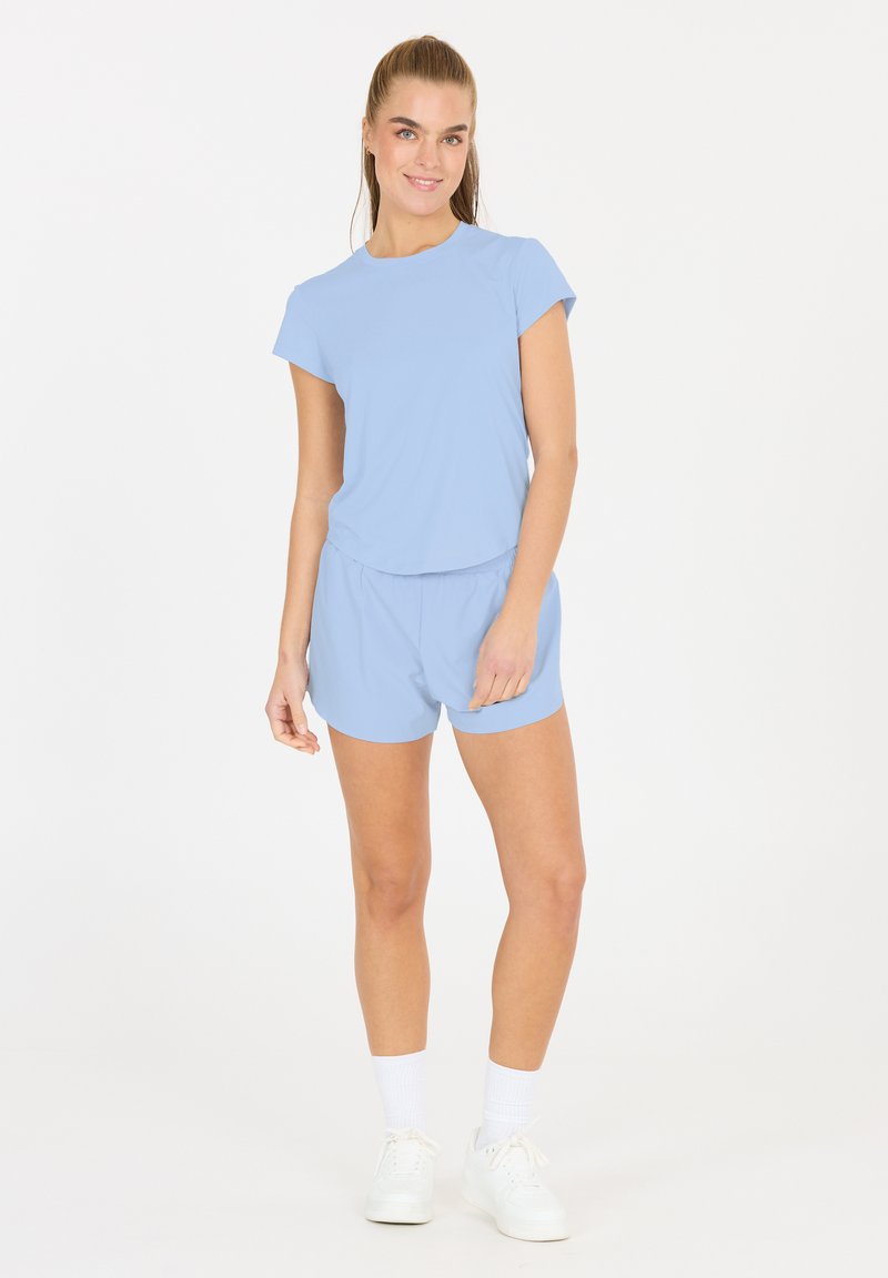 Helles blaues Sportoberteil und Shorts-Set aus weichem Material, mit kurzen Ärmeln und elastischem Bund für Komfort. Weiße Turnschuhe und Socken.