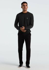 Grau gestrickter Pullover mit Rundhalsausschnitt, gerippten Bündchen und Saum; schwarze Slim-Fit-Hose und schwarze Sneaker mit weißen Sohlen.