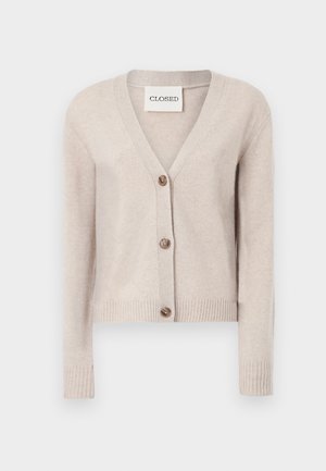 Gilet en cachemire beige avec un col en V, des poignets côtelés et une rangée de quatre boutons marron sur le devant. L'étiquette indique "CLOSED".