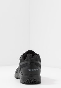Zapatilla deportiva negra con malla texturizada y superposiciones sintéticas. Cuenta con una suela de goma y la marca "Reebok" en el lateral.