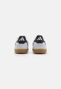 Chaussures de sport blanches avec des accents noirs et un logo à trois bandes. Semelles en caoutchouc texturé, talon rembourré et semelle en gomme contrastante. Vue arrière montrée.