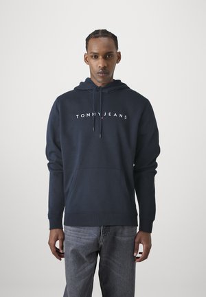 Marineblauwe hooded sweatshirt met een voorste kangoeroe-pocket en witte "TOMMY JEANS" tekstlogo over de borst.