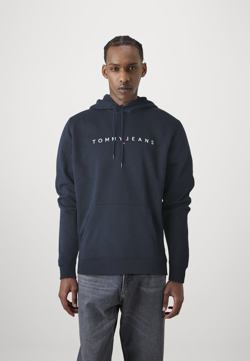 Felpa con cappuccio blu navy caratterizzata da una tasca a marsupio frontale e logo bianco "TOMMY JEANS" sul petto.