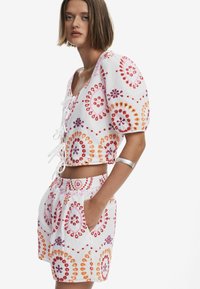 Vitt tvådelat set bestående av en kortärmad topp med puffärmar och snörning fram, dekorerad med färgglada cirkulära mönster, samt matchande shorts med fickor.