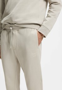 Μπεζ φόρμα με ελαστική μέση με κορδόνι, πλαϊνό τσεπάκι που κρατάει το χέρι και μικρό τετράγωνο λογότυπο "BOSS" στον μηρό.