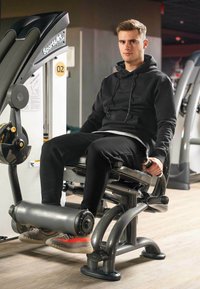 Macchina per estensione delle gambe in una palestra, con un sedile imbottito nero e le gambe sostenute da un cuscino cilindrico grigio. Presenta un robusto telaio metallico e maniglie.