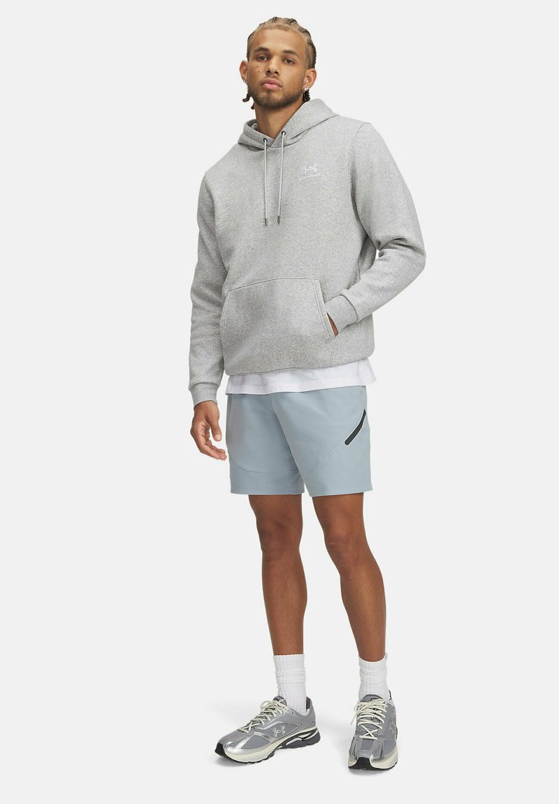 Sudadera gris claro con cordones ajustables y un bolsillo canguro, combinada con pantalones cortos azul claro que tienen un bolsillo con cremallera lateral. Zapatillas deportivas.