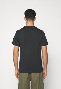 Svart bomullströja med rund halsringning och korta ärmar, med en slät yta och en enkel design. Bärs tillsammans med olivgröna cargo-byxor.