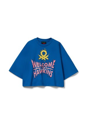 Camiseta azul recortada de manga corta, con un diseño gráfico que dice "WELCOME TO HAWKINS" en rosa con acentos amarillos. Tela suave.