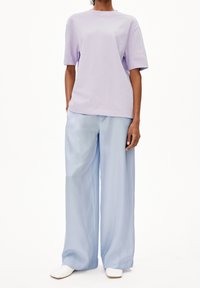 Ljuslila bomullströja med korta ärmar, kombinerad med vida ljusblå byxor i ett flödande material, och vita slip-on skor.