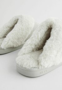 Faux fur slippers in soft white; plush upper, wide opening, padded footbed, and a textured rubber sole with "NEXT" embossed on the side.