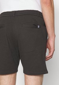 Shorts en coton gris foncé avec une taille élastique, deux poches arrière et un ourlet replié. Le tissu a une texture douce.