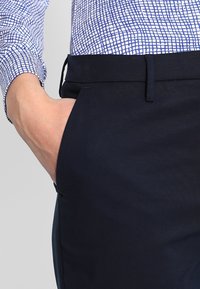 Mörkblå byxor med slim fit, med flat front, sidofickor och en slät yta. Bärs med en mönstrad skjorta.